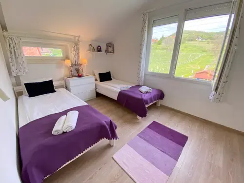 Szépvölgyi Vendégház két ágyas szobája lila takarókkal és fekete párnákkal